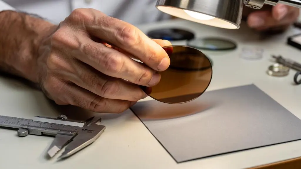 Un opticien examine la transparence d'un verre teinté marron au-dessus de son plan de travail.